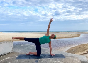 Ascension Editing Instructor Annie doing side plank balancing on one knee and one hand at the beach.